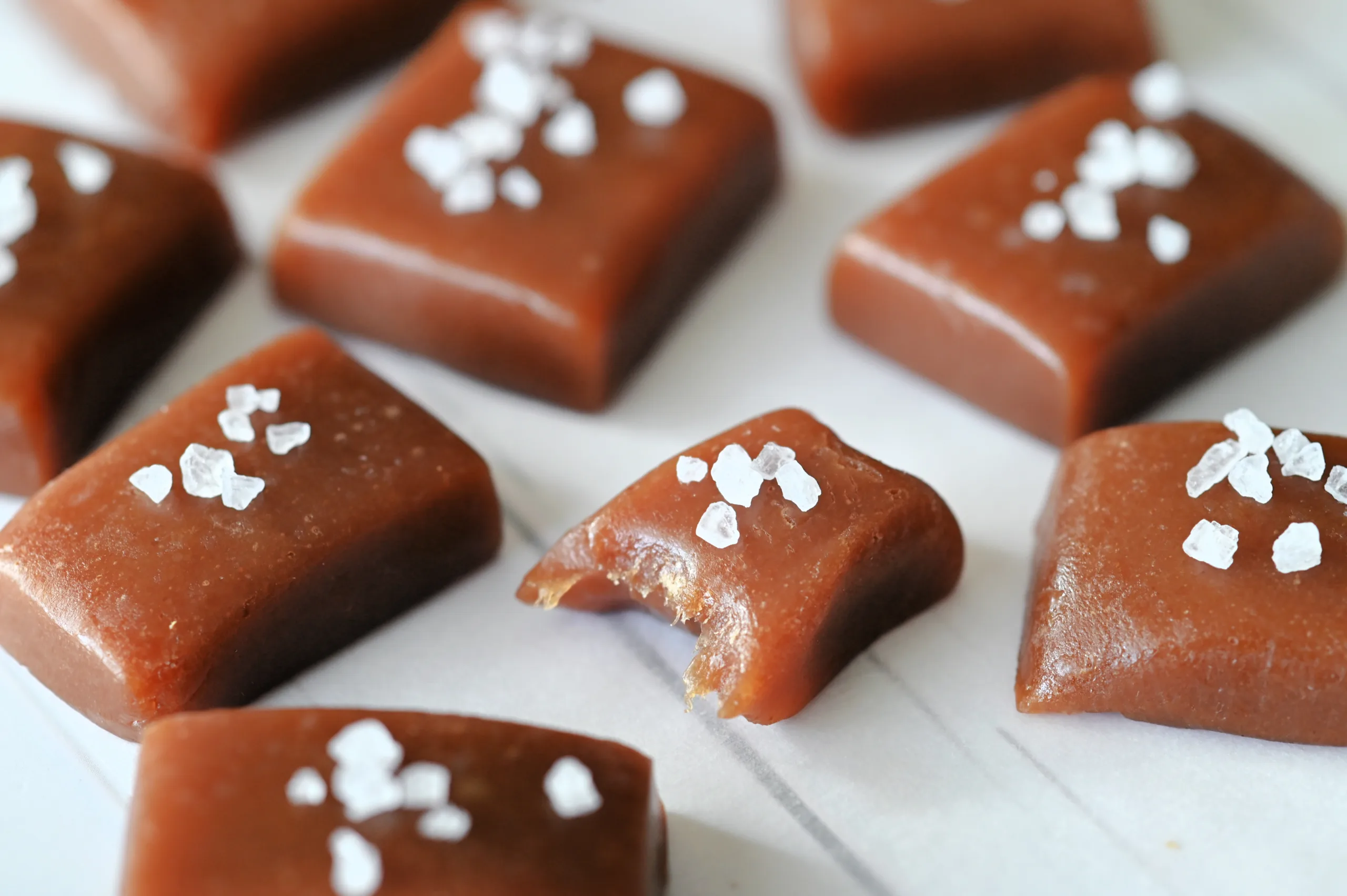 Soft chewy caramel candies with flaky sea salt, including one piece with a bite taken out.