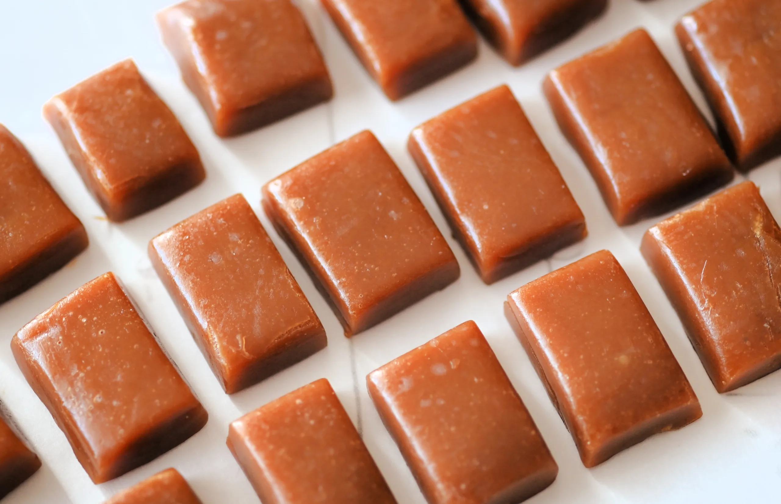 Homemade caramel candy cut into small squares on parchment paper.