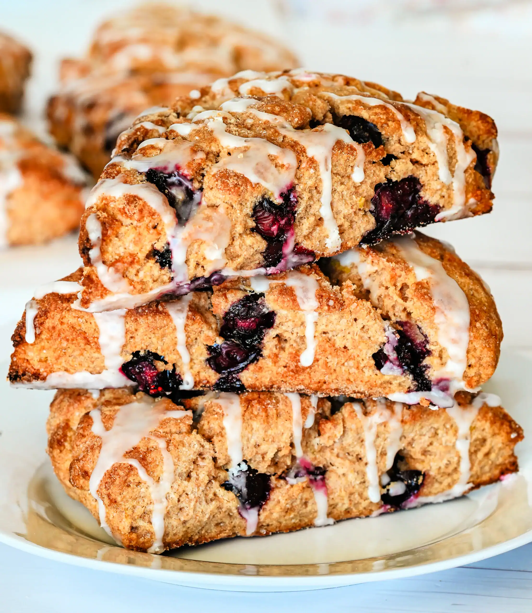 Homemade lemon blueberry scones drizzled with lemon glaze, golden brown and filled with fresh blueberries, stacked on a plate for a cozy breakfast or brunch.