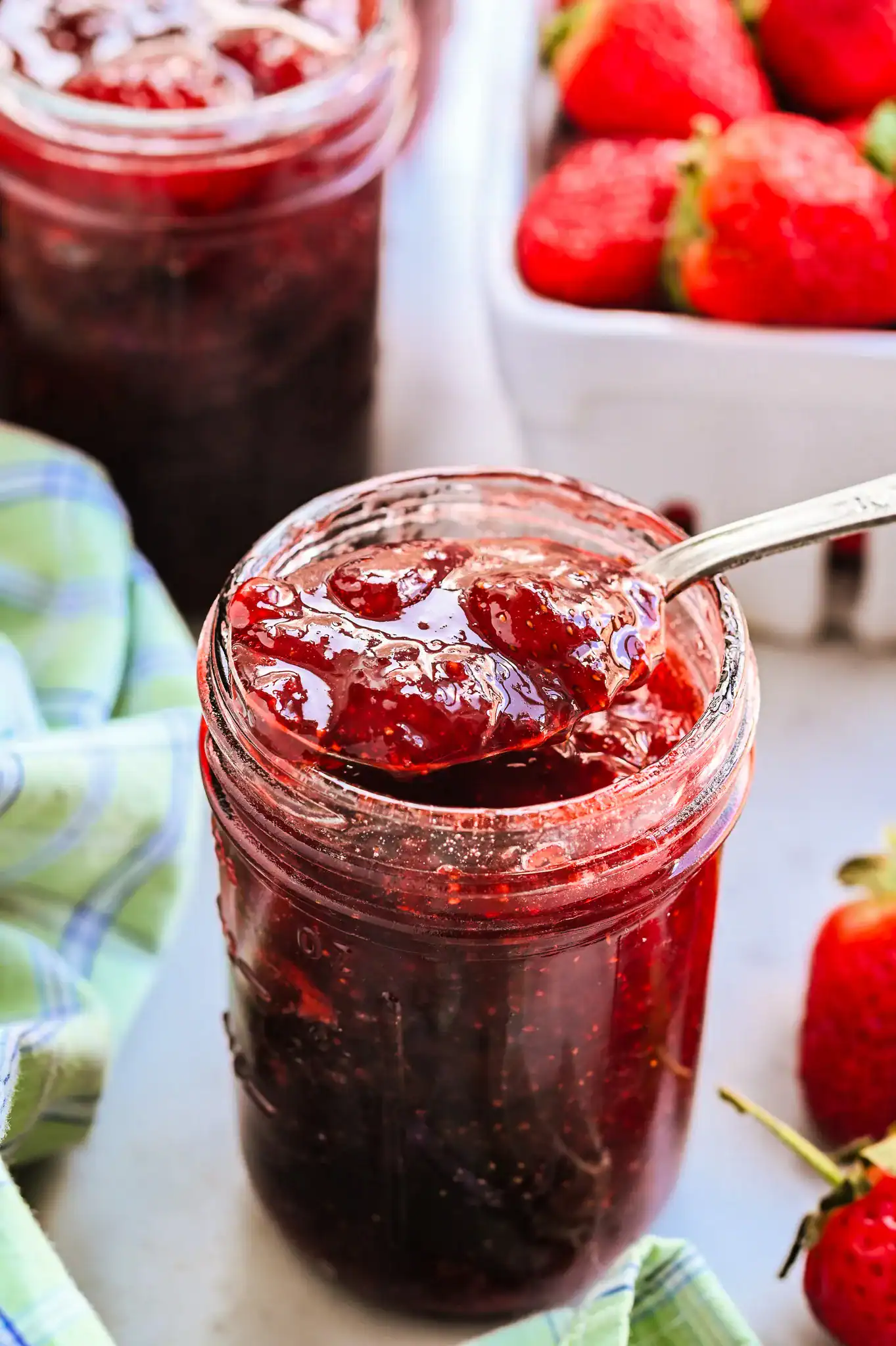 Homemade strawberry jam in a glass mason jar with spoon, surrounded by fresh strawberries, no pectin, small batch recipe.