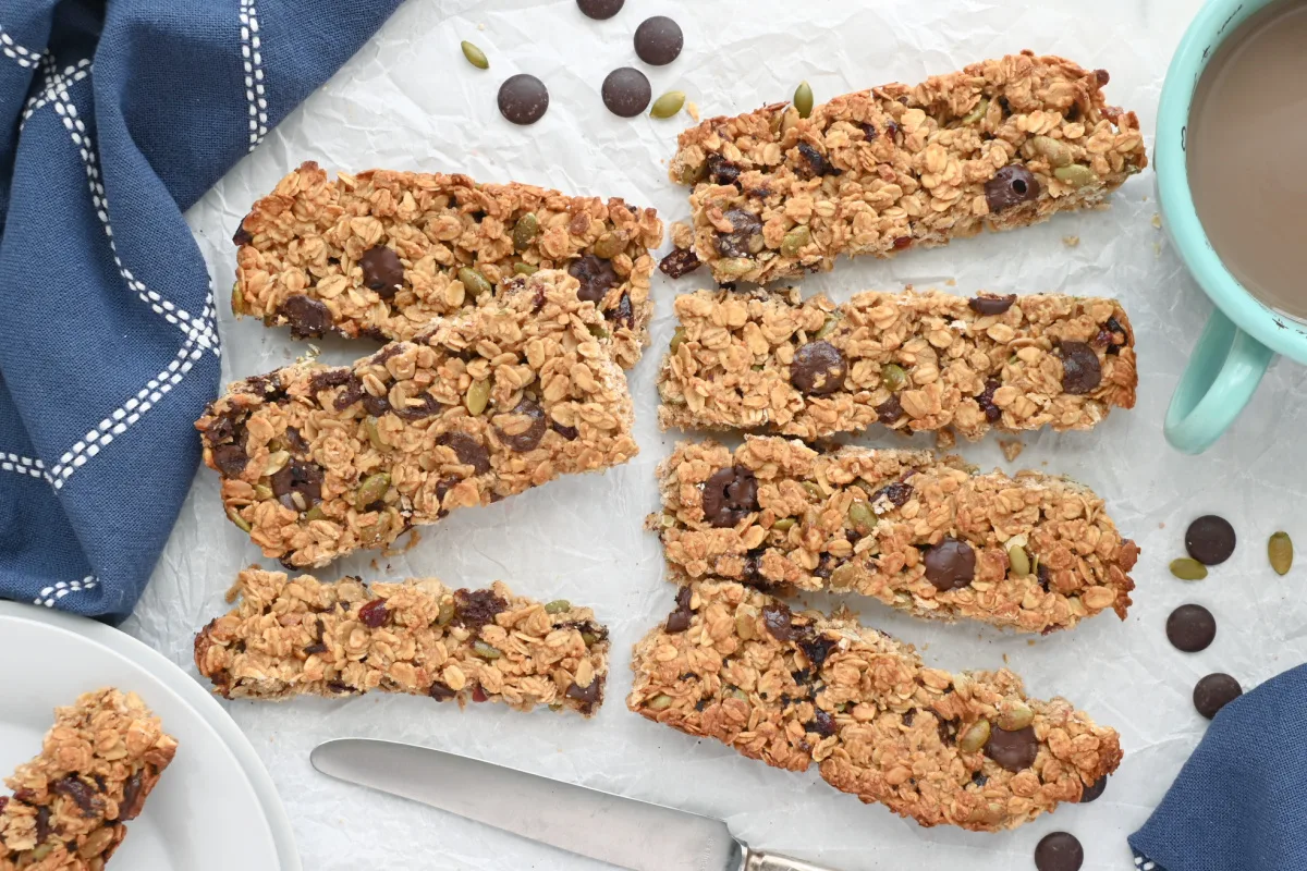 Top view of sliced chewy granola bars made with oats, sourdough discard, dark chocolate chips, pumpkin seeds, and dried fruit, arranged on parchment paper with a mug of coffee