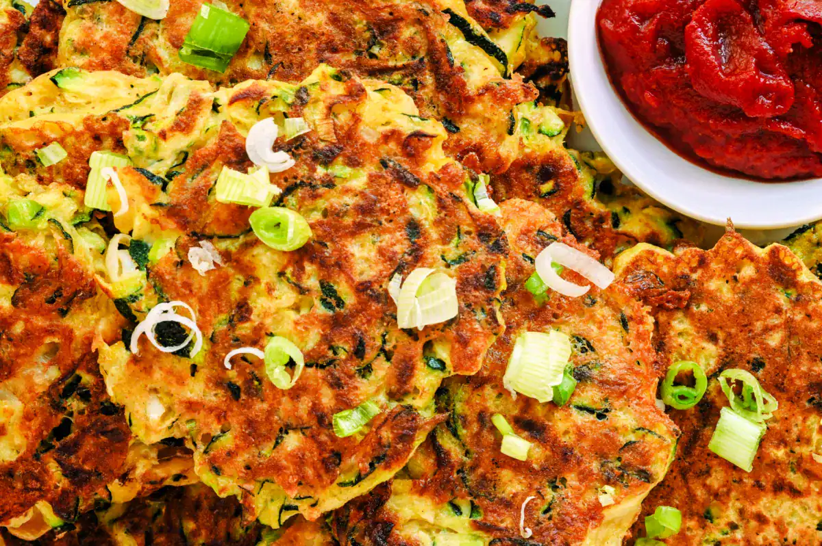 Stacks of homemade zucchini fritters on a white plate, garnished with green onions and served with dipping sauce – easy, kid-friendly sourdough discard recipe.