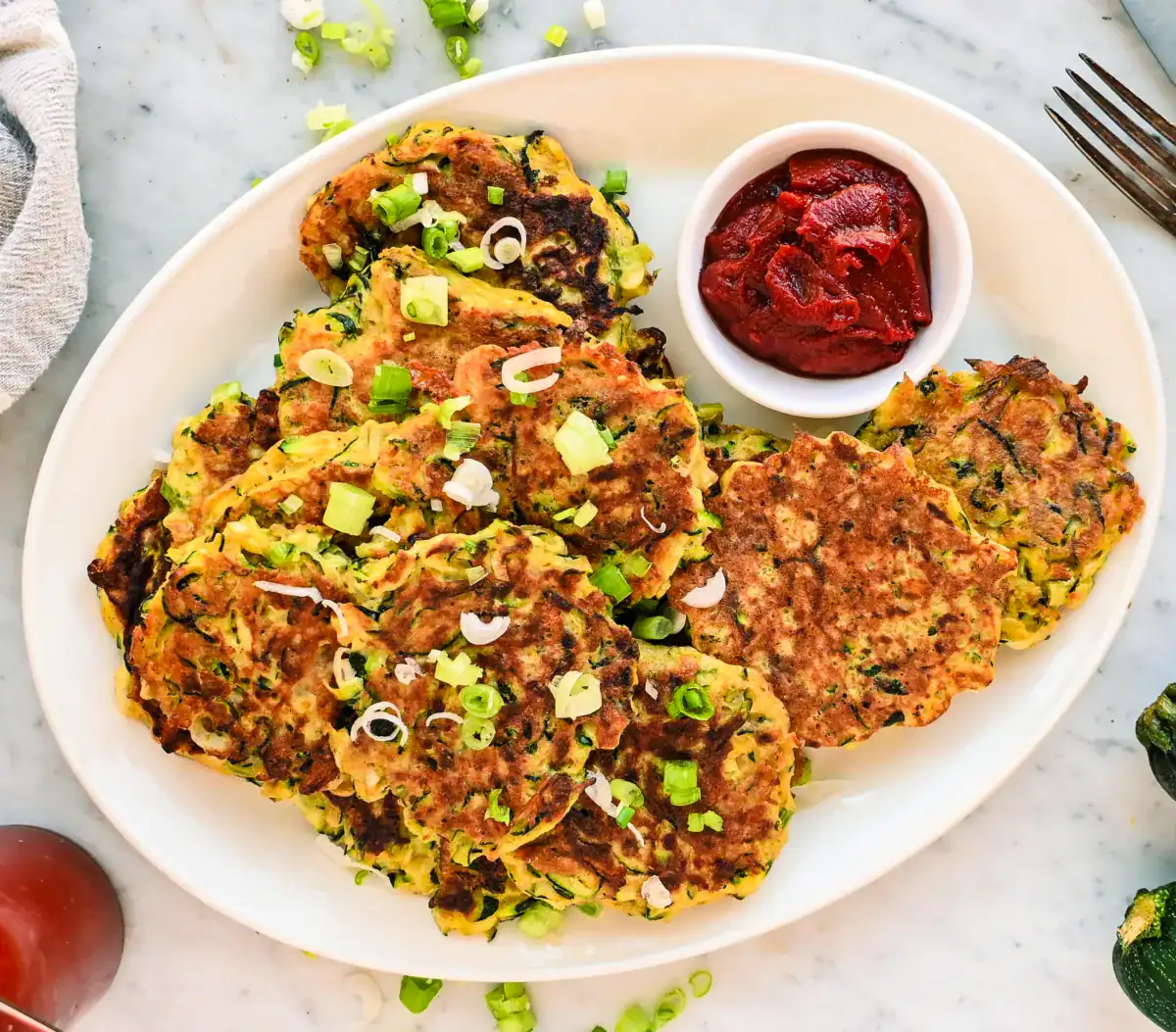 Stacks of homemade zucchini fritters on a white plate, garnished with green onions and served with dipping sauce – easy, kid-friendly sourdough discard recipe.