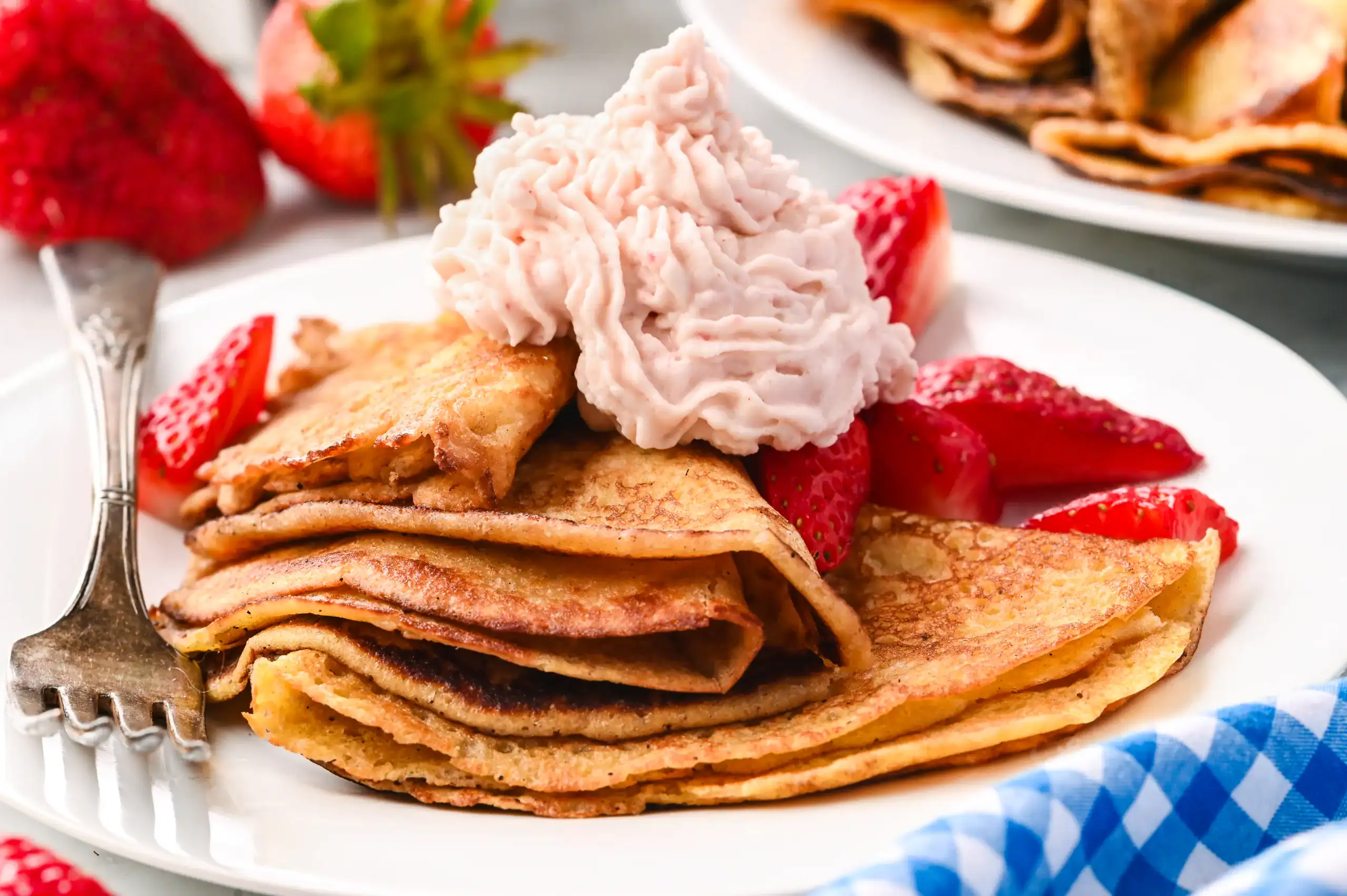 Plate of thin, golden sourdough crepes stacked with fresh strawberries and a swirl of strawberry whipped cream, served with a fork.