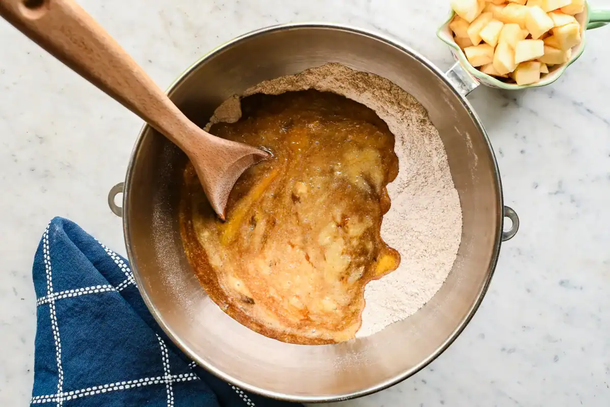 Mixing sourdough discard batter with wooden spoon in a large bowl, ready to add chopped apples for muffins.
