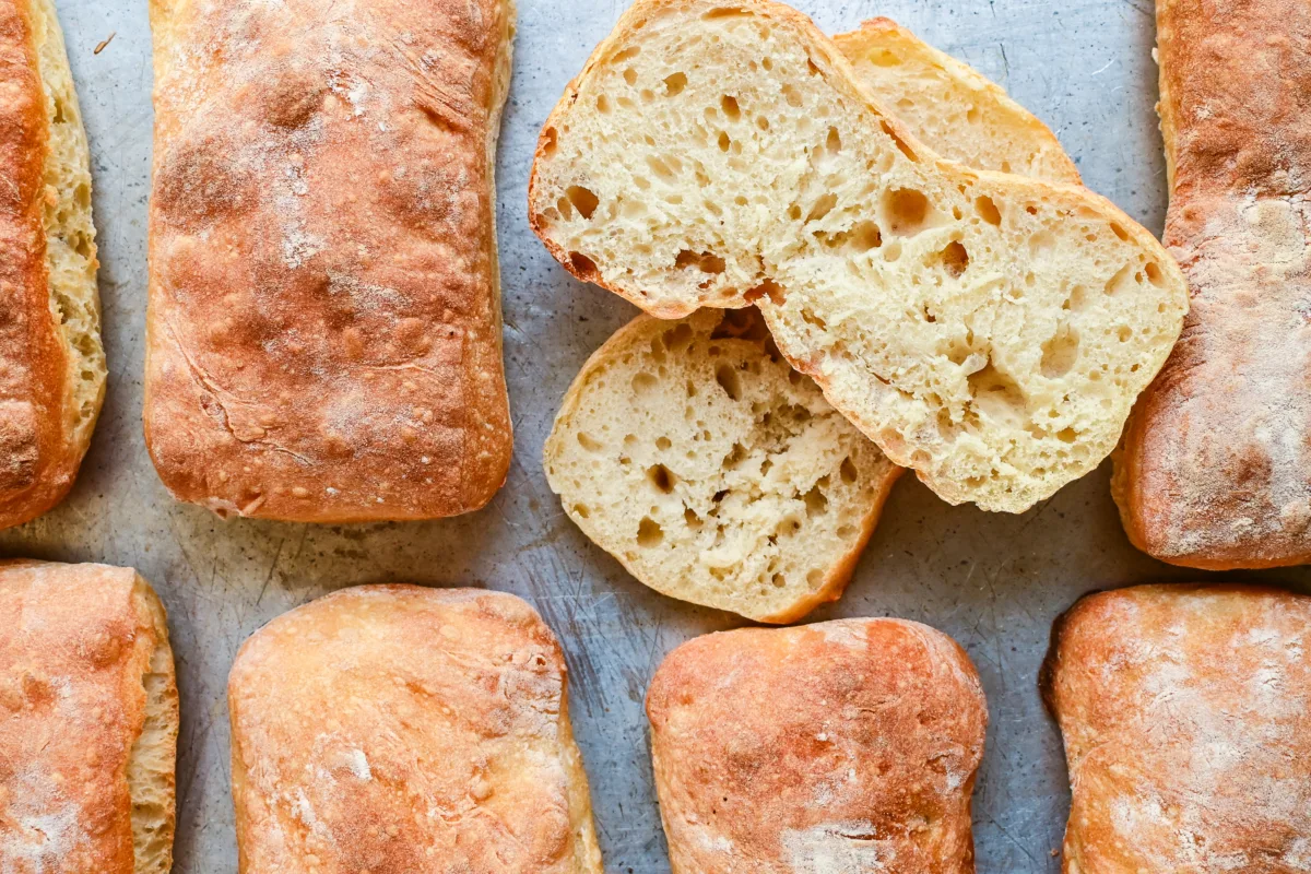 Golden brown sourdough ciabatta rolls fresh from the oven, baked to perfection on a lined tray.