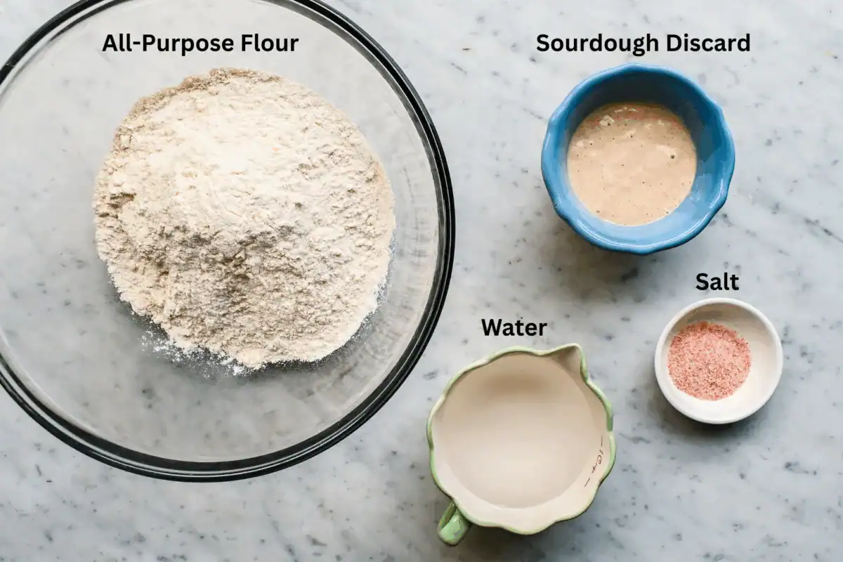 Overhead view of sourdough discard, flour, water, and pink salt being mixed in a glass bowl to start ciabatta dough.