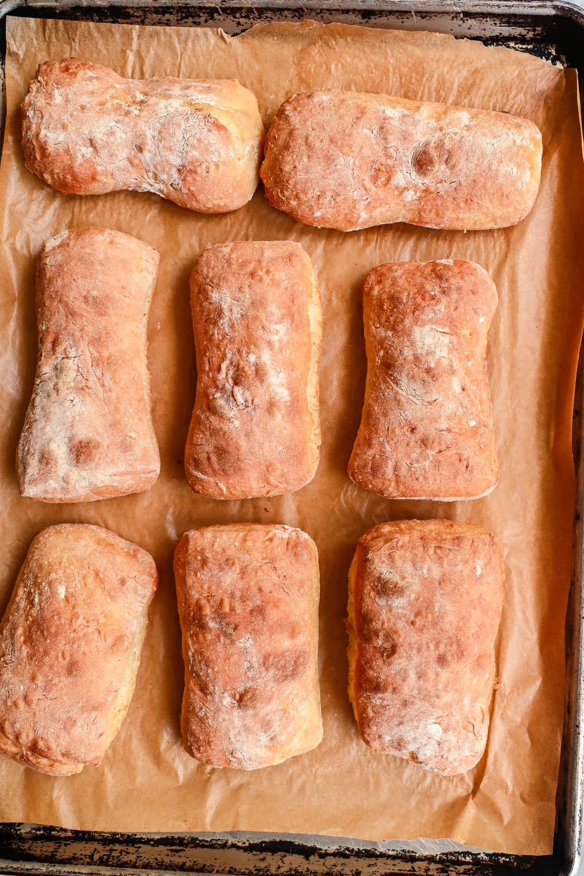 Golden brown sourdough ciabatta rolls fresh from the oven, baked to perfection on a lined tray.