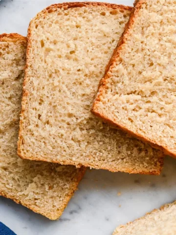 Sliced sourdough sandwich bread with a soft, fluffy crumb and lightly golden crust, baked in a loaf pan and arranged on a marble surface for an everyday homemade sandwich bread recipe.