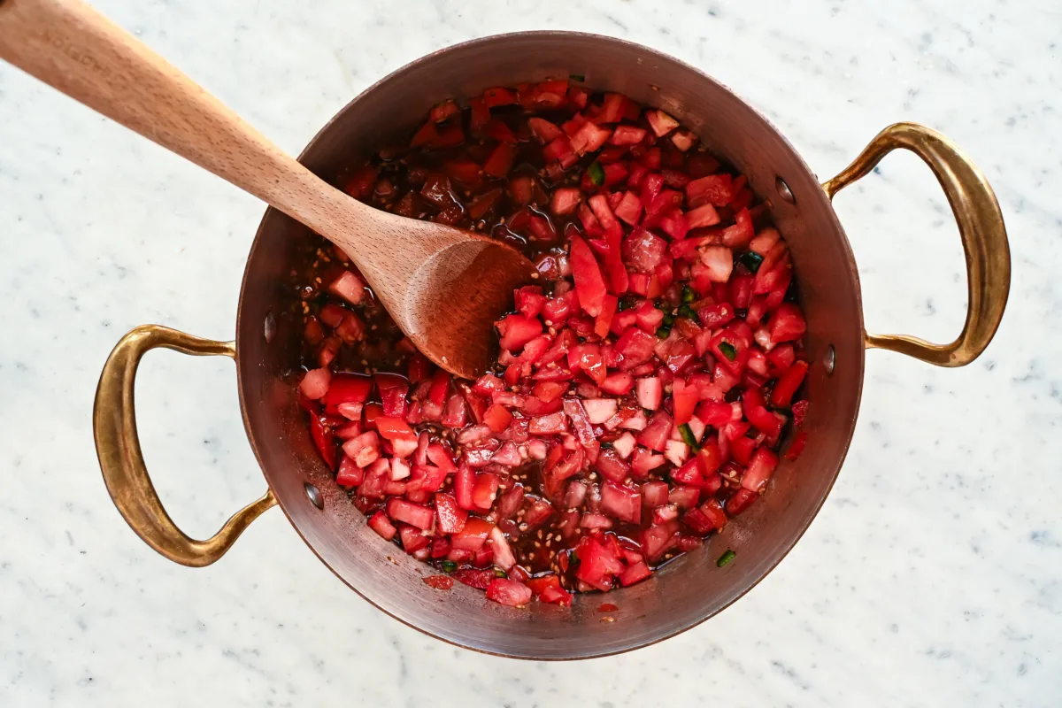 Tomato jam ingredients being stirred in a pot as they begin to cook down and release flavor.