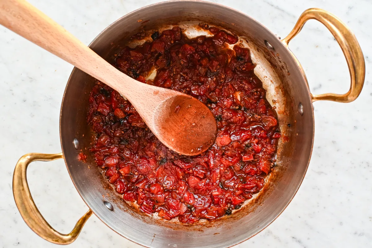 Thickened tomato jam mixture in a pot after simmering, showing its rich texture and deep color.