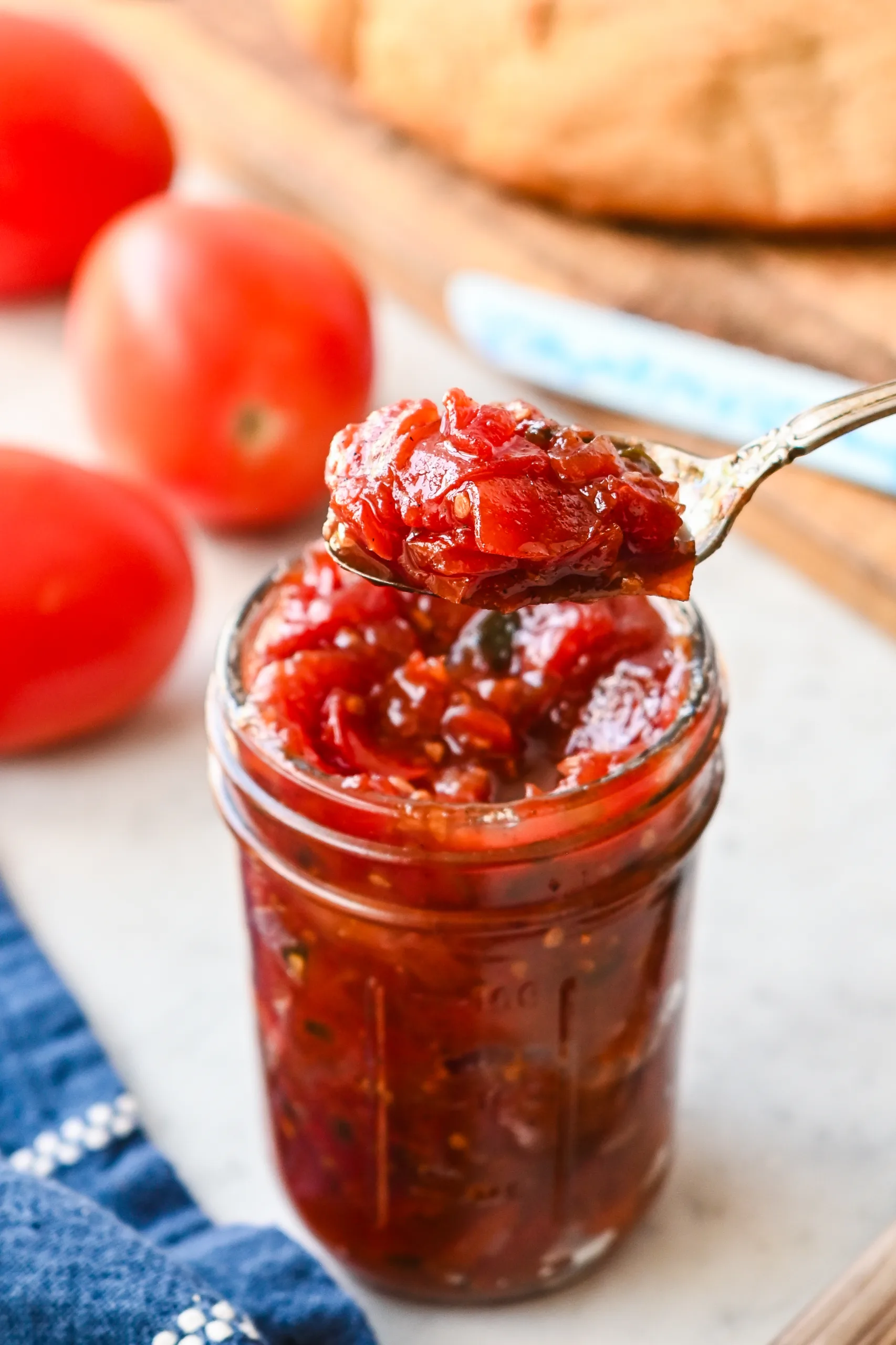 Close-up of tomato jam being scooped from a mason jar, highlighting its chunky, jammy consistency.