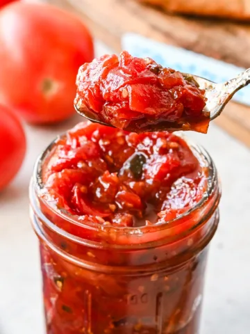 Close-up of tomato jam being scooped from a mason jar, highlighting its chunky, jammy consistency.