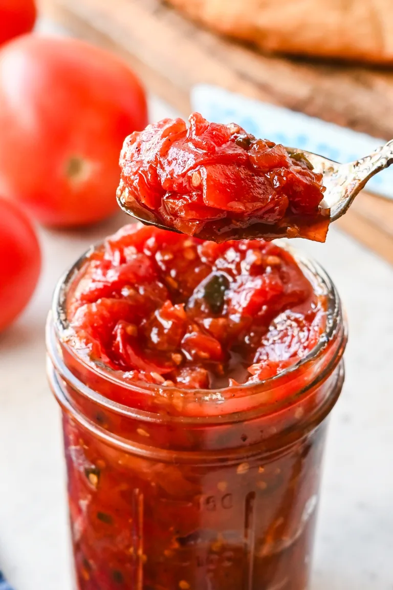 Close-up of tomato jam being scooped from a mason jar, highlighting its chunky, jammy consistency.
