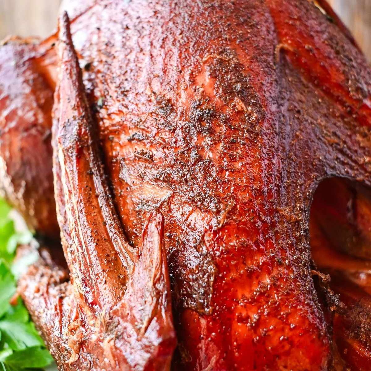 Whole pellet smoked turkey with crispy golden-brown skin, seasoned and served on a white platter with fresh parsley