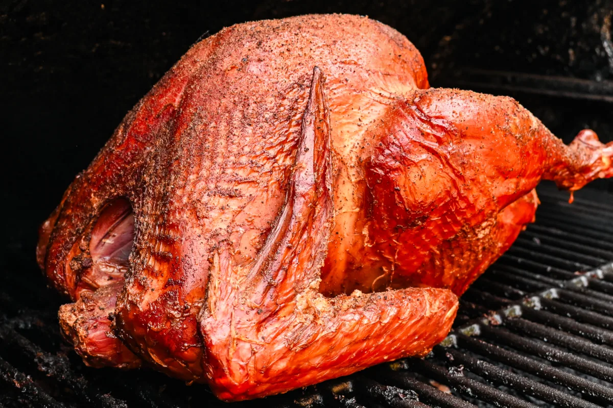 Whole pellet smoked turkey with crispy golden-brown skin, seasoned and served on a pellet smoker being smoked.