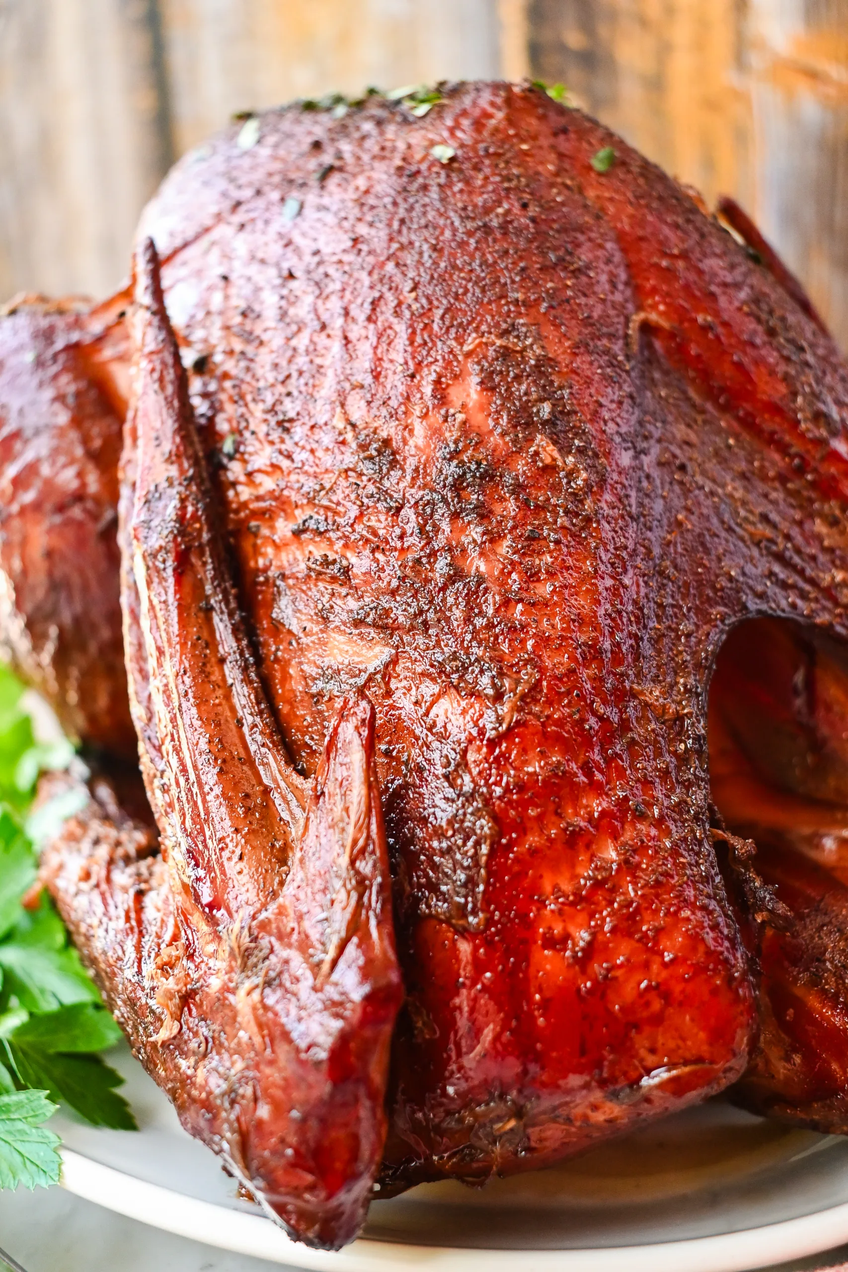 Whole pellet smoked turkey with crispy golden-brown skin, seasoned and served on a white platter with fresh parsley