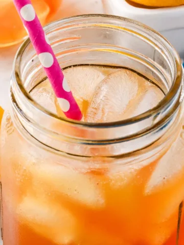 Refreshing glass of homemade switchel over ice with a pink straw, served in a mason jar.