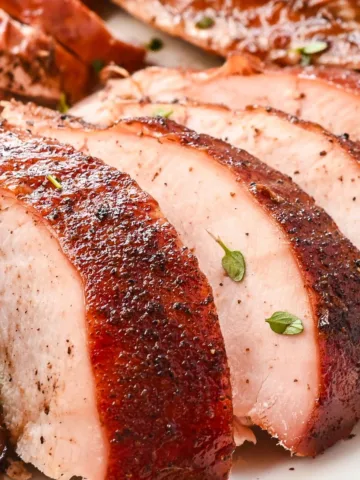 Juicy sliced smoked turkey breast with crispy skin and fresh herbs on a serving platter.