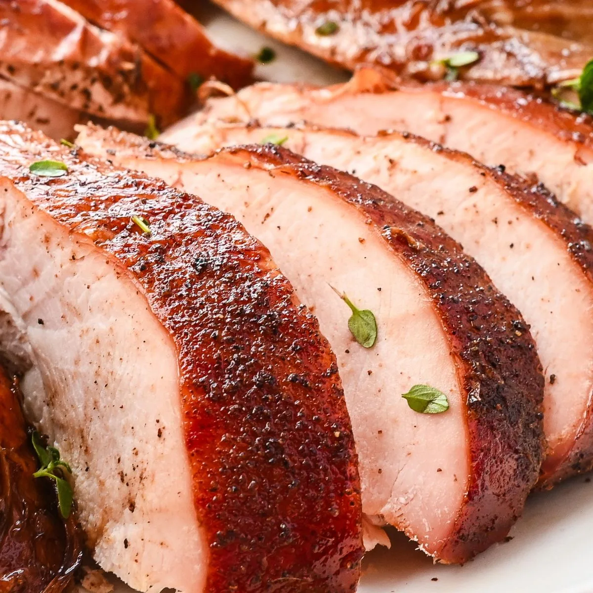 Juicy sliced smoked turkey breast with crispy skin and fresh herbs on a serving platter.