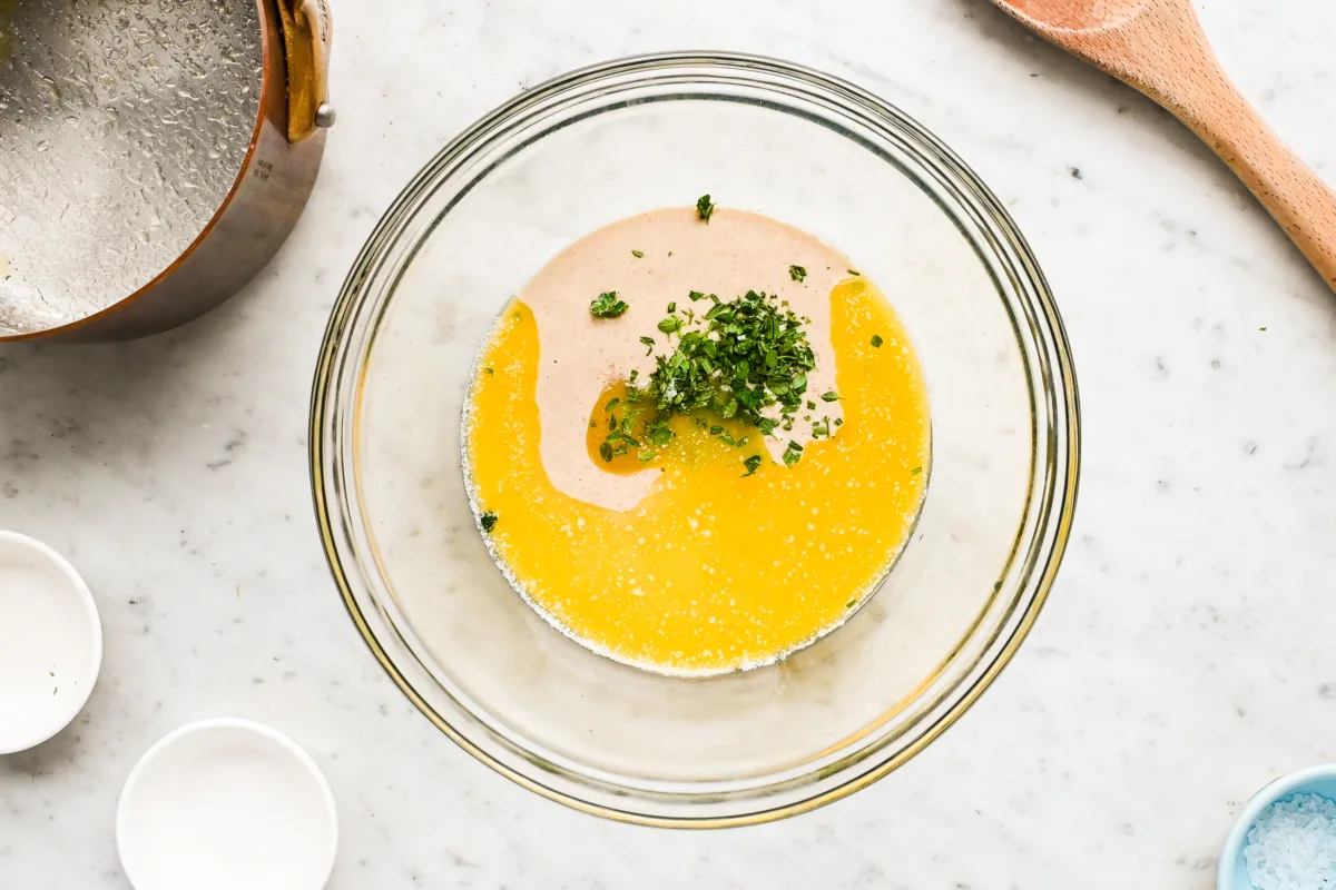 Mixing sourdough cracker dough with fresh herbs using a wooden spoon in a glass bowl—an easy recipe using unfed sourdough starter.