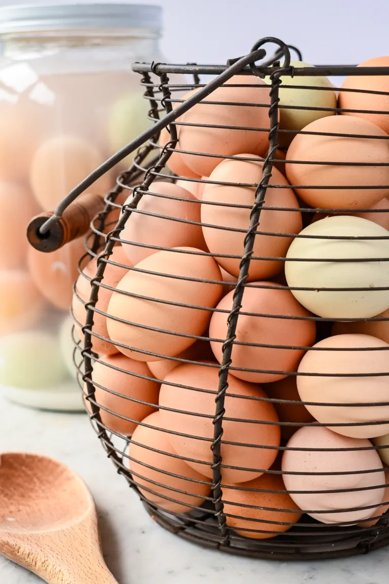 Wire egg basket filled with colorful homestead eggs, with water-glassed eggs in a jar in the background.