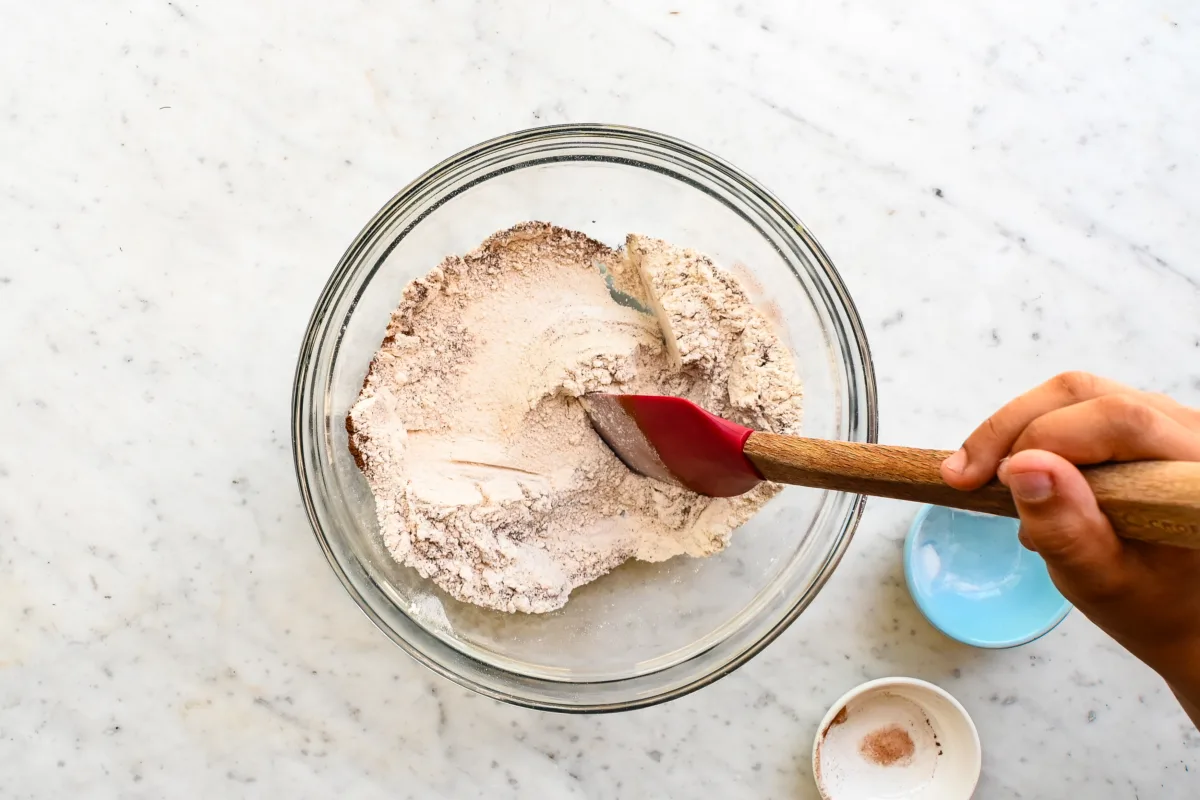 Mixing dry ingredients including fresh milled flour, cinnamon, and salt in a glass bowl for oatmeal raisin cookie dough.