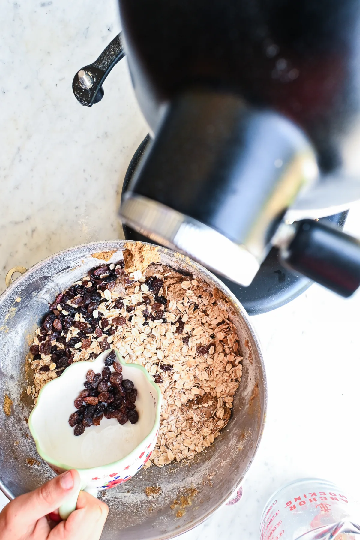 Folding raisins and rolled oats into cookie dough inside a stand mixer bowl.