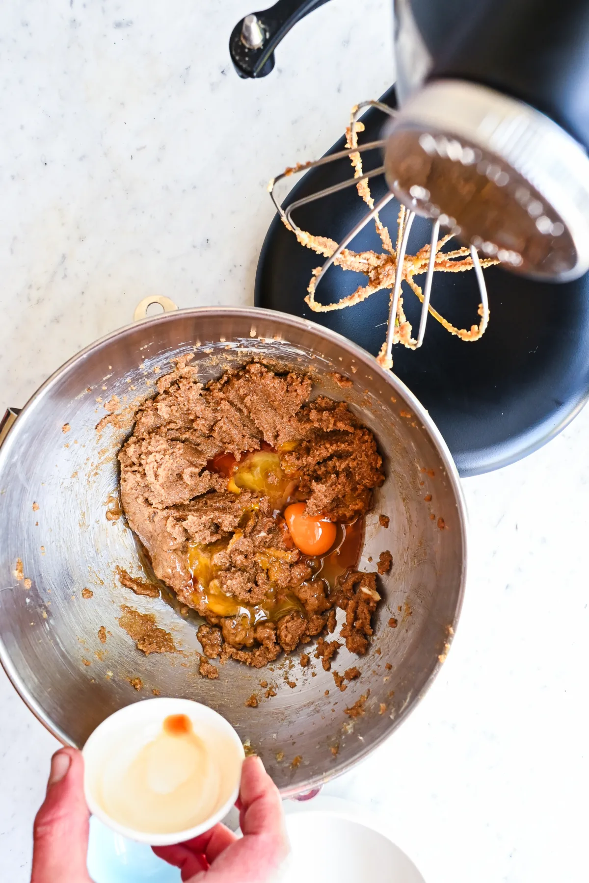 Cracking eggs and adding vanilla extract to creamed butter and sugar in a stand mixer bowl.