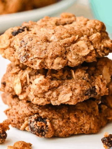 Freshly baked healthy oatmeal raisin cookies stacked on a white plate with a mug in the background.