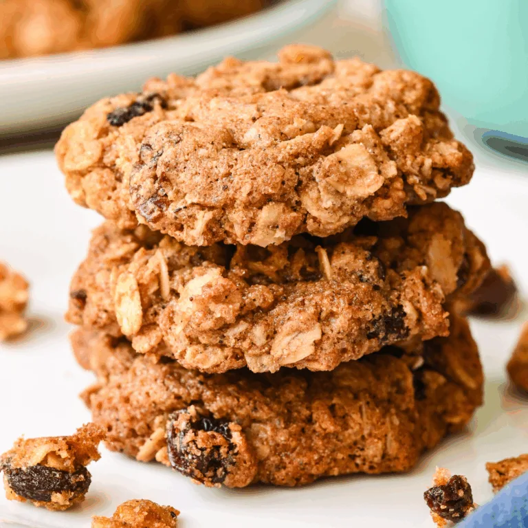 Freshly baked healthy oatmeal raisin cookies stacked on a white plate with a mug in the background.