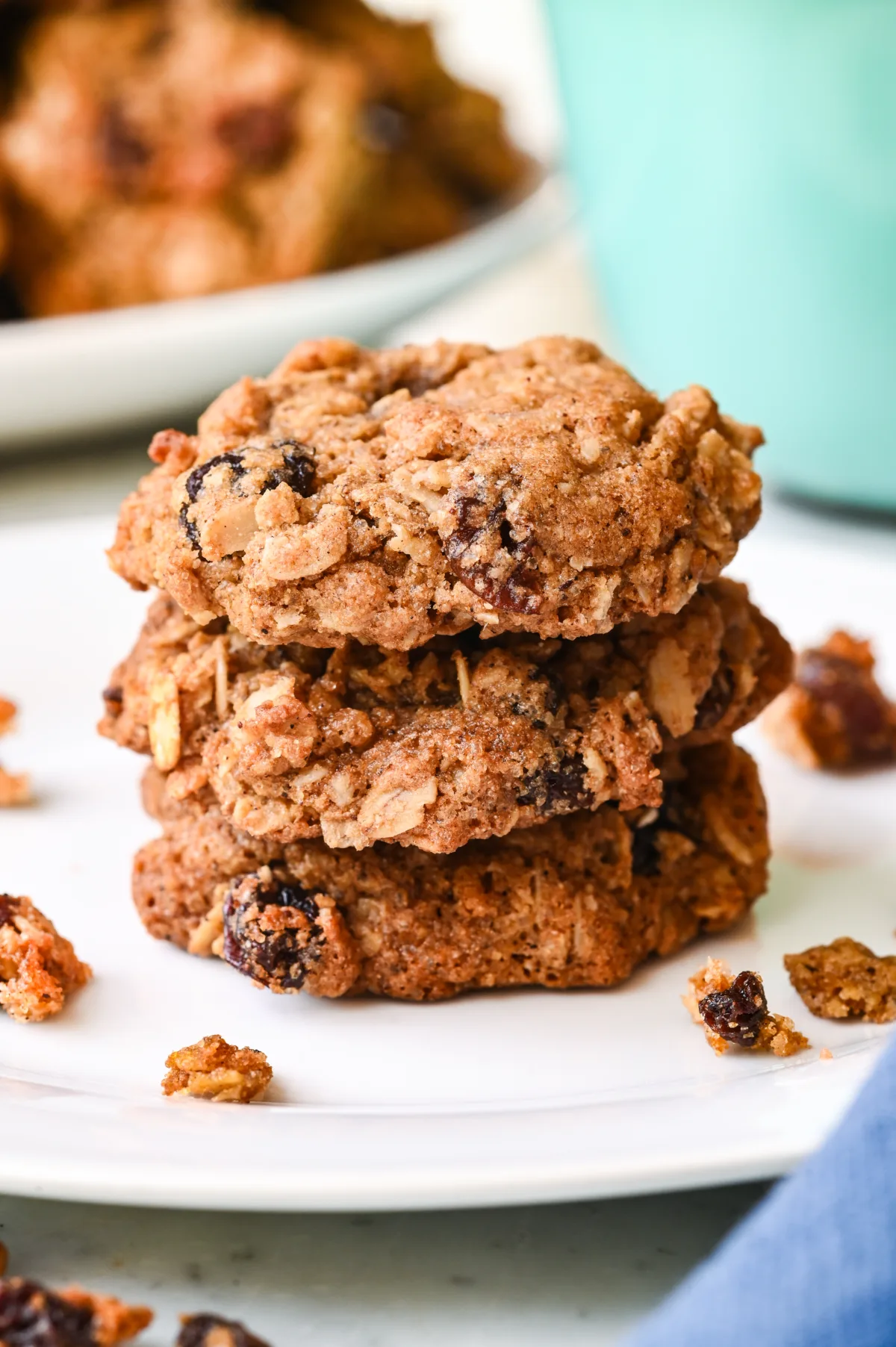 Freshly baked healthy oatmeal raisin cookies stacked on a white plate with a mug in the background.