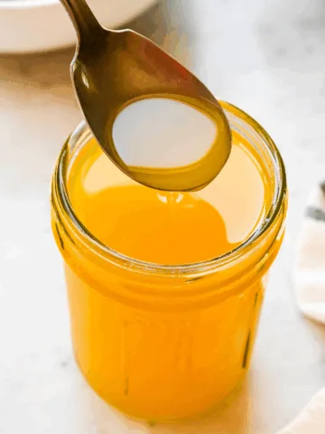 Spoon dipped into a jar of homemade ghee, showing its rich golden color and smooth texture.