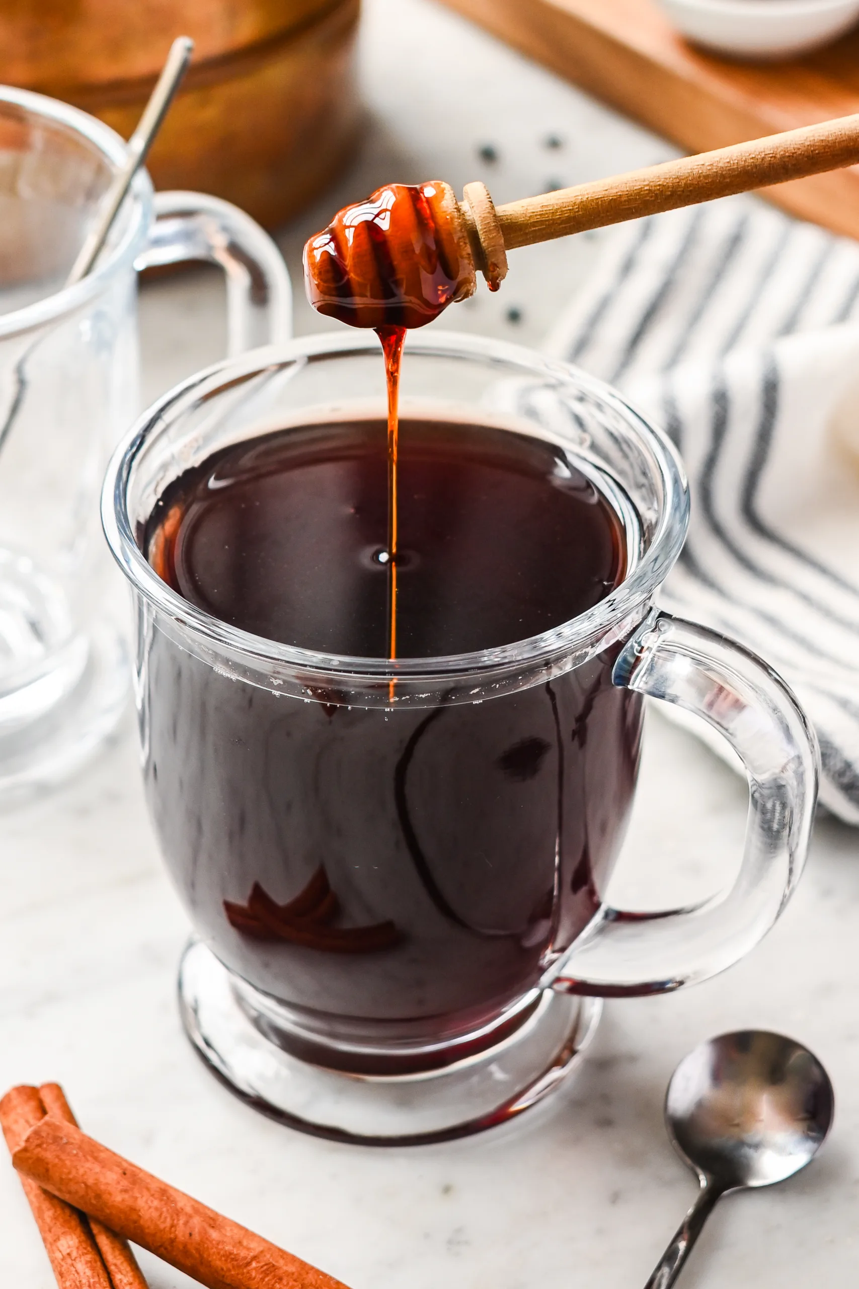 Glass mug of hot elderberry tea sweetened with raw honey, an herbal tea known for its immune-boosting properties, with cinnamon sticks on the side.