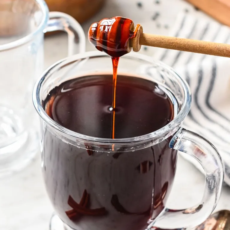 Glass mug of hot elderberry tea sweetened with raw honey, an herbal tea known for its immune-boosting properties, with cinnamon sticks on the side.