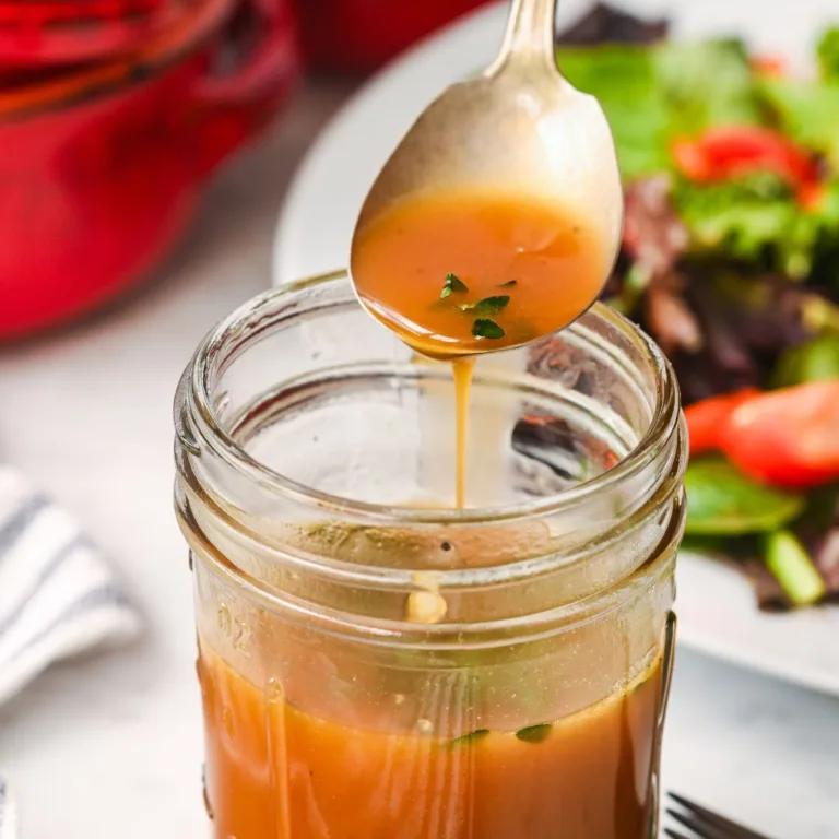 Spoon drizzling homemade salad dressing with fresh herbs from a mason jar over a green salad.