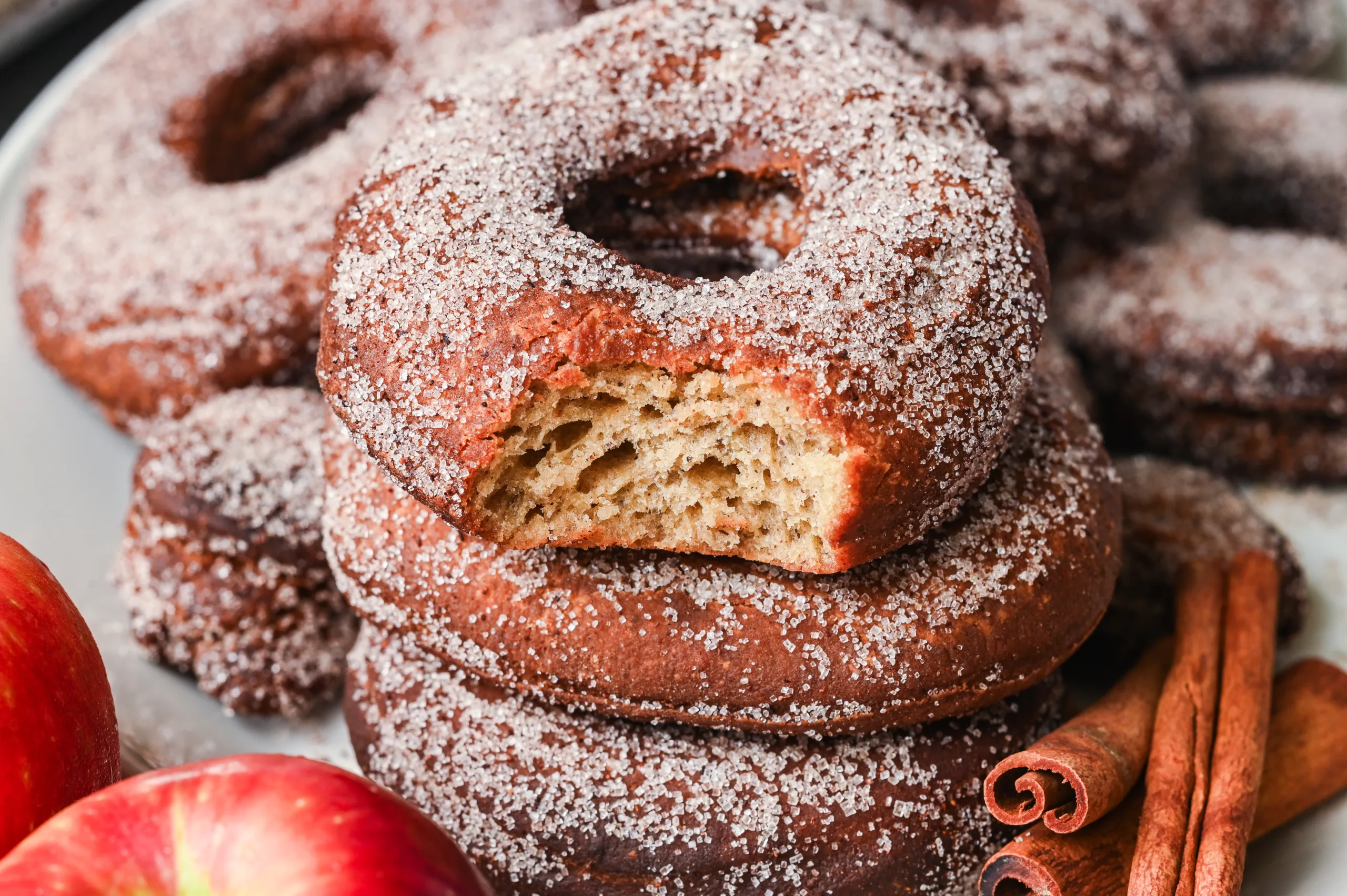 Stack of cinnamon sugar-coated sourdough apple cider donuts, one with a bite showing fluffy interior.