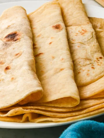 Plate of homemade sourdough tortillas folded and stacked, golden and soft, ready to serve.