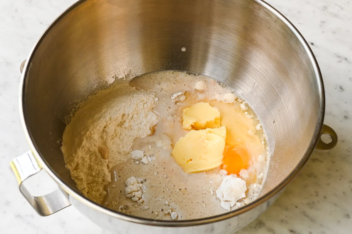 Mixing flour, butter, egg, sourdough discard, and other ingredients in the bowl of a stand mixer for soft sourdough rolls.