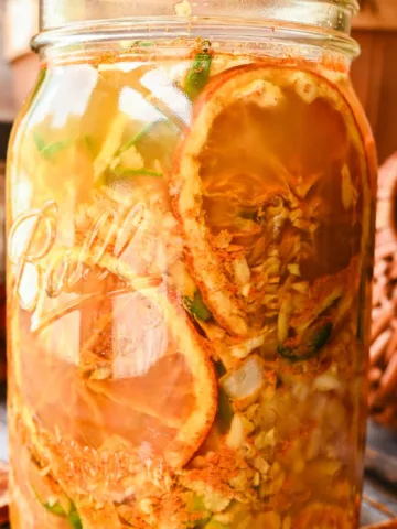 Close-up of a jar filled with homemade fire cider tonic, showcasing vibrant layers of dried orange slices, ginger, jalapeños, and herbs steeping in apple cider vinegar.