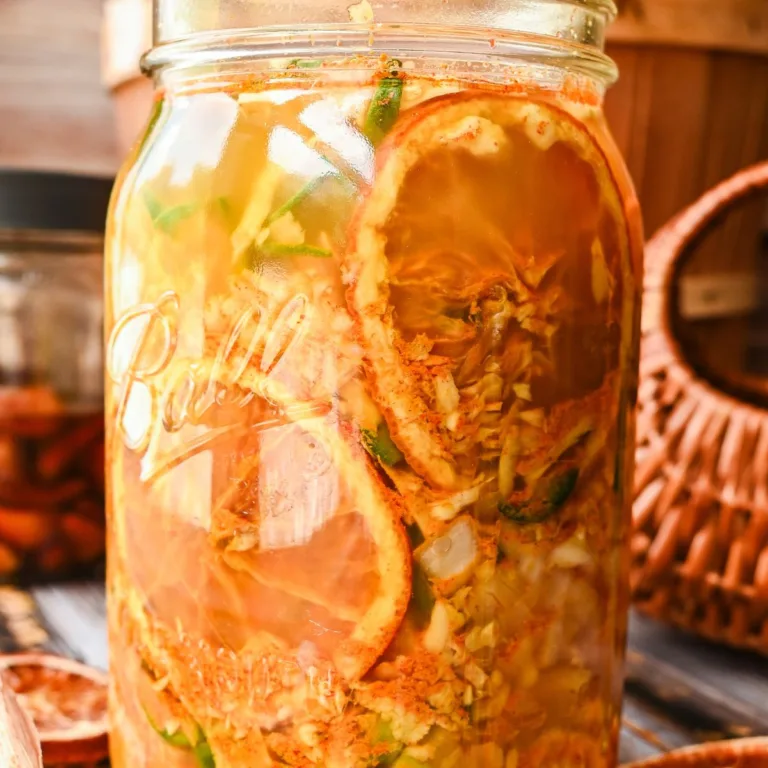 Close-up of a jar filled with homemade fire cider tonic, showcasing vibrant layers of dried orange slices, ginger, jalapeños, and herbs steeping in apple cider vinegar.