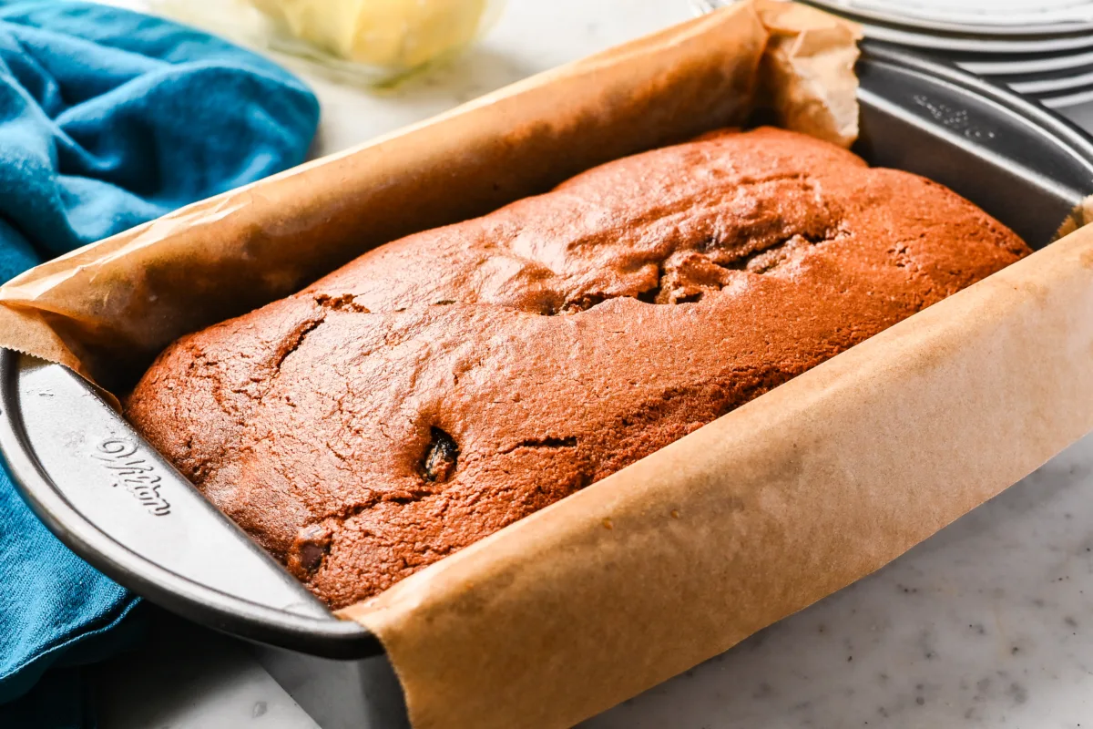 Freshly baked sourdough cherry chocolate chip quick bread in a parchment-lined loaf pan, golden brown on top.