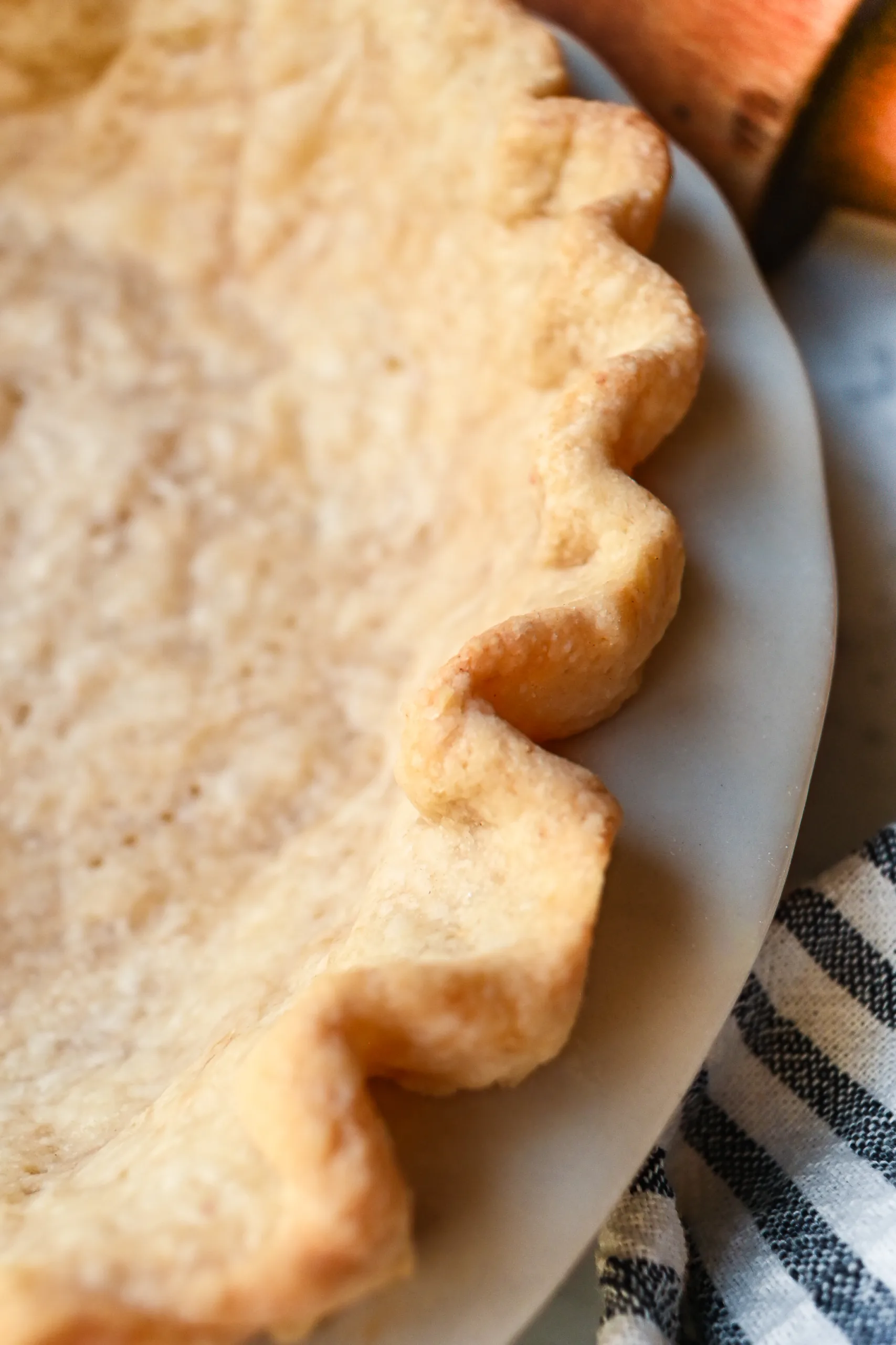 Golden baked sourdough pie crust with crimped edges and fork holes, cooling in a white pie dish on a marble surface with a rolling pin nearby.