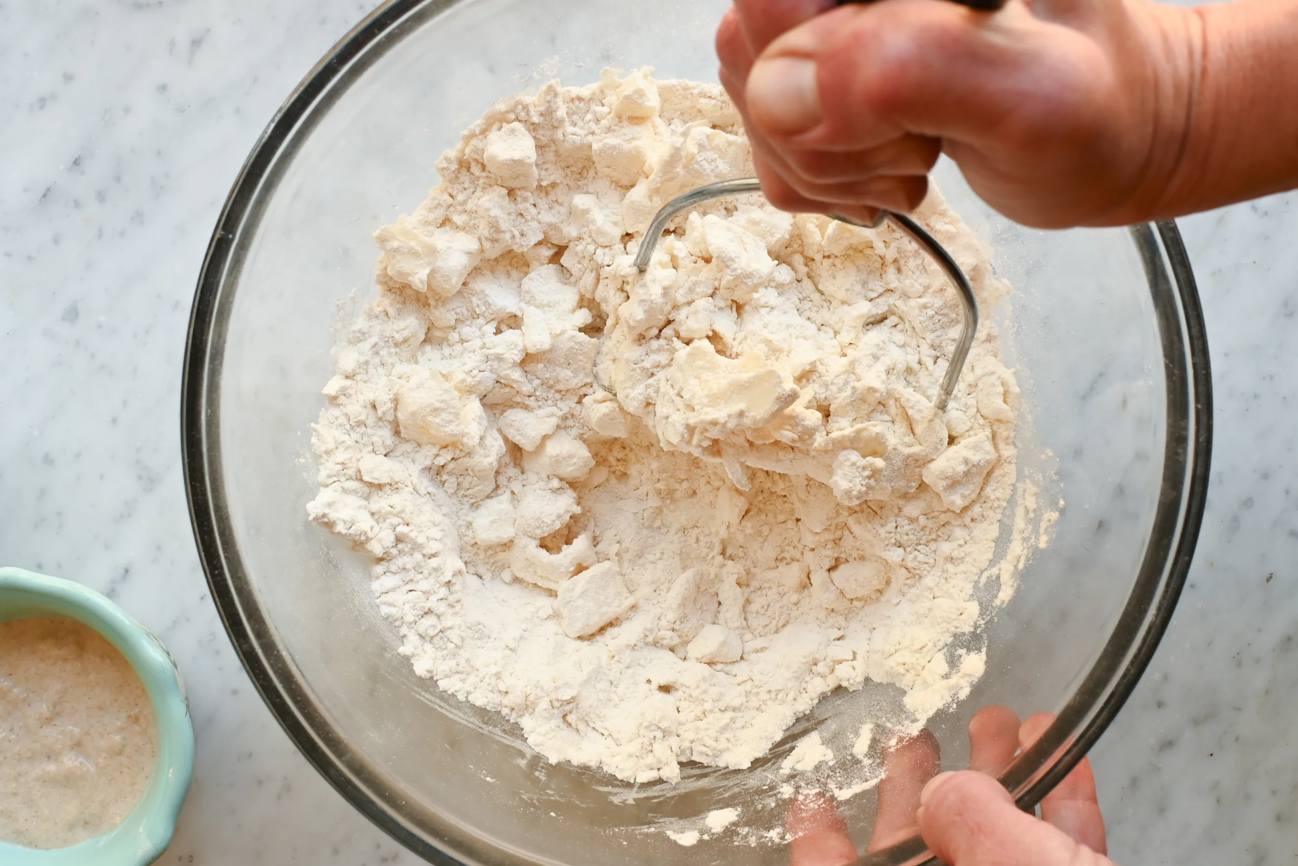 Using a pastry cutter to work butter into the flour mixture for sourdough pie crust until coarse crumbs form.