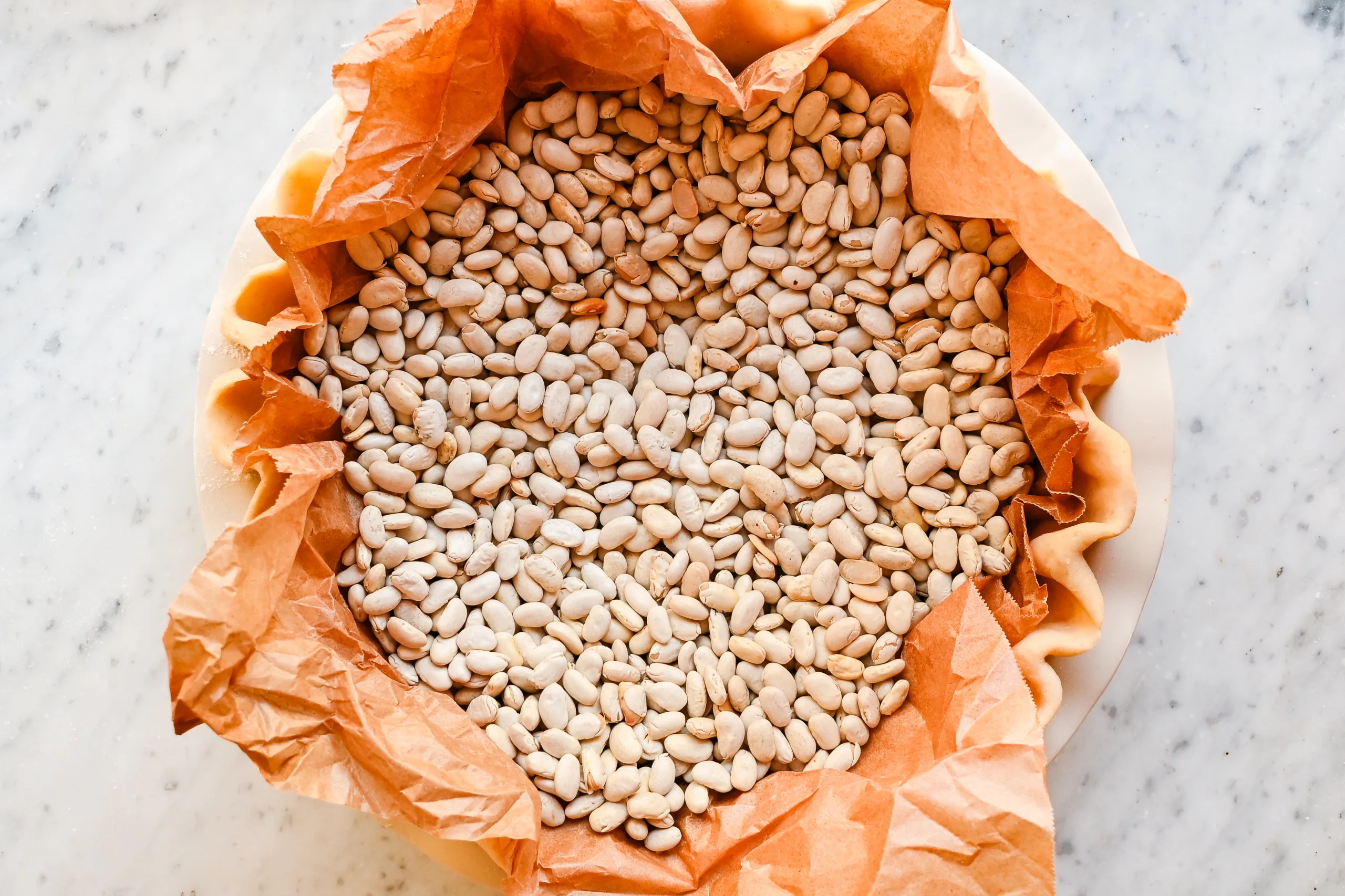 Pie shell lined with parchment paper and filled with dried beans for blind baking.