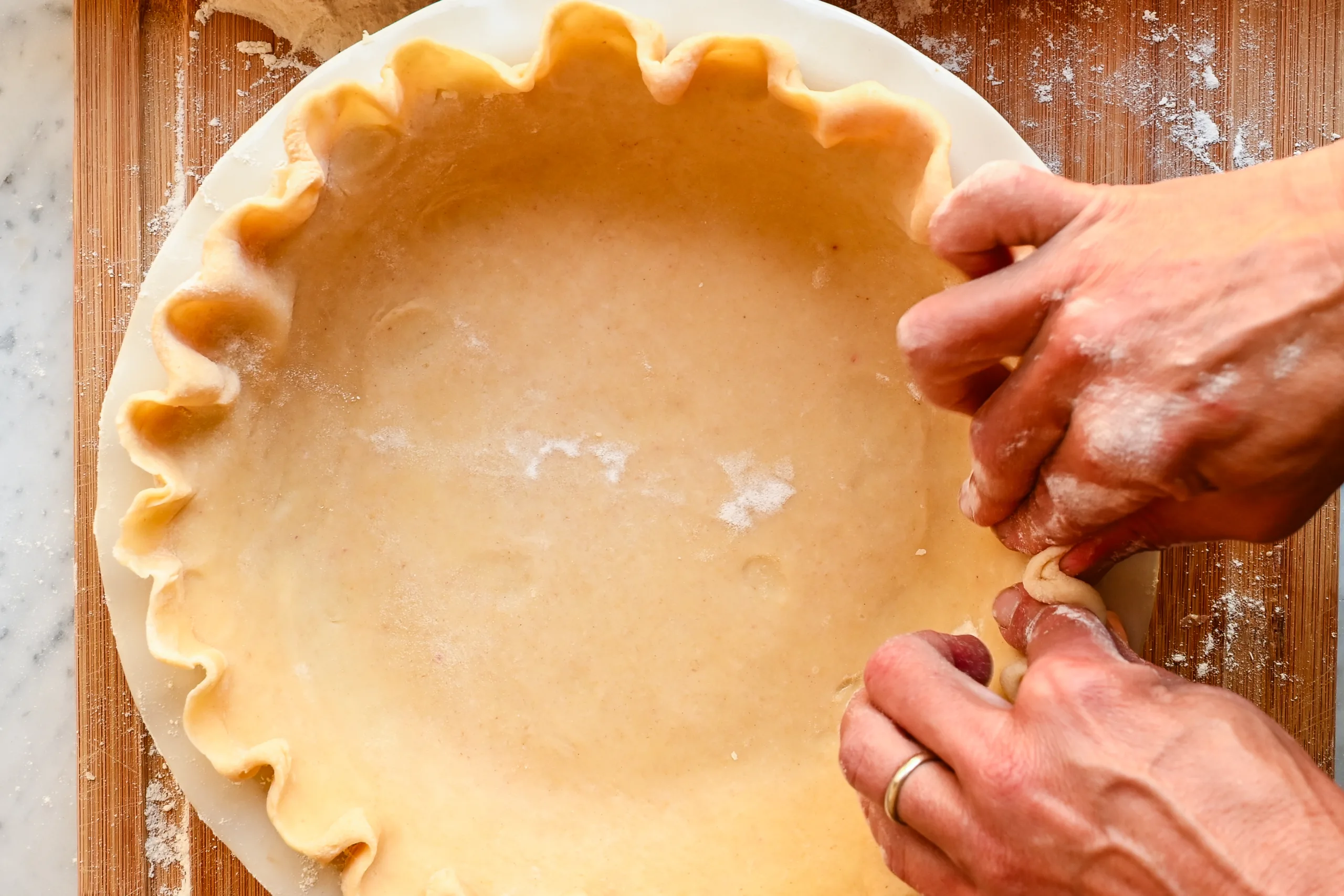 Shaping and crimping the edges of sourdough pie crust dough in a pie plate.