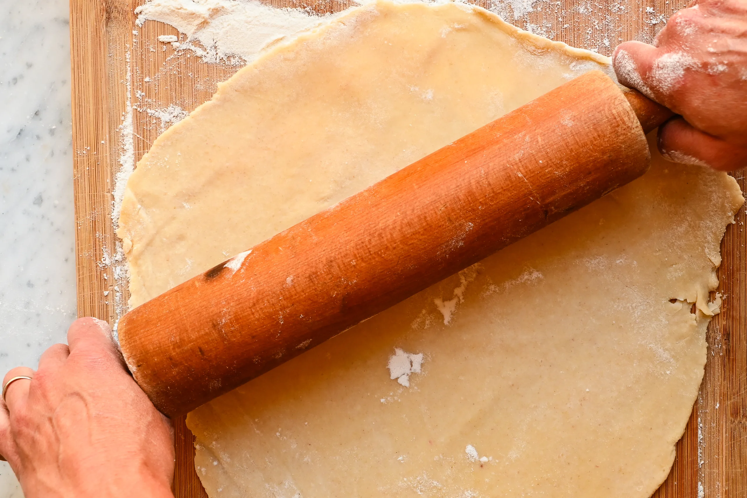 Rolling sourdough pie crust dough with a wooden rolling pin on a floured surface.
