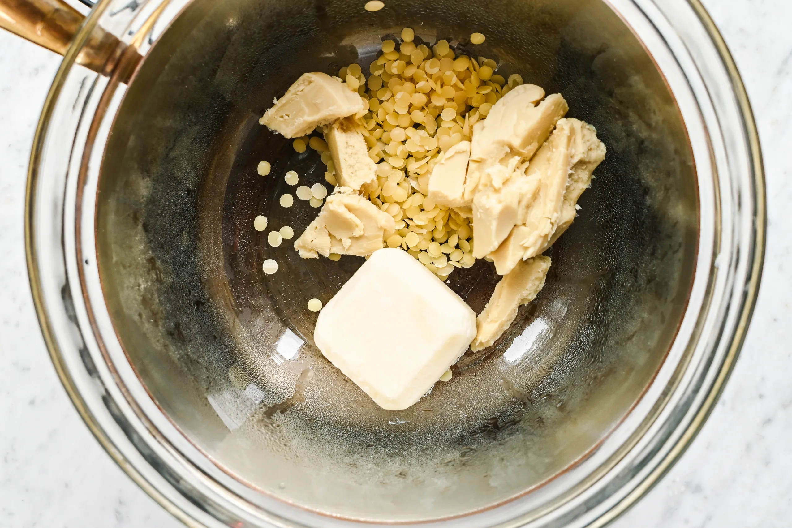 Beeswax pellets, tallow, and shea butter placed together in a double boiler bowl, ready to be melted for DIY lip balm.