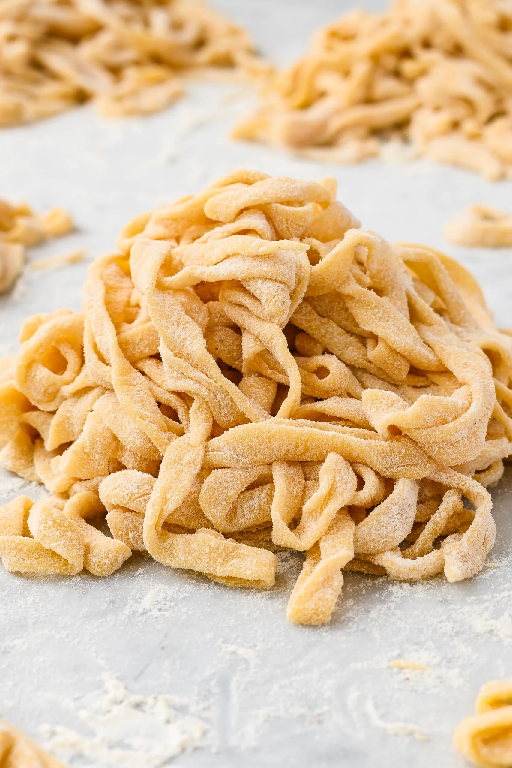 Freshly cut sourdough pasta noodles coated in flour and piled on a work surface, ready for drying or cooking.