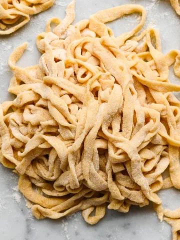 Floured nests of fresh sourdough pasta noodles on a marble surface, ready to cook or store for later use.